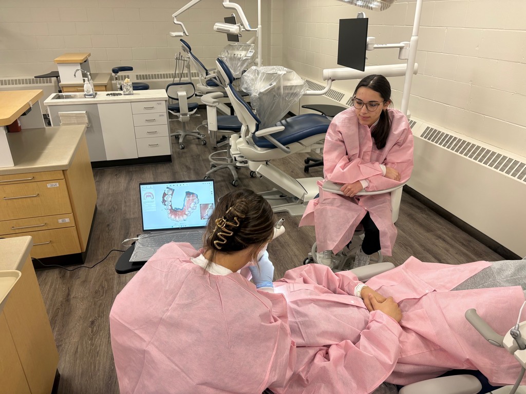 Student using a 3Shape TRIOS scanner to capture a 3D digital model/scan of classmate's teeth with another student observing them.