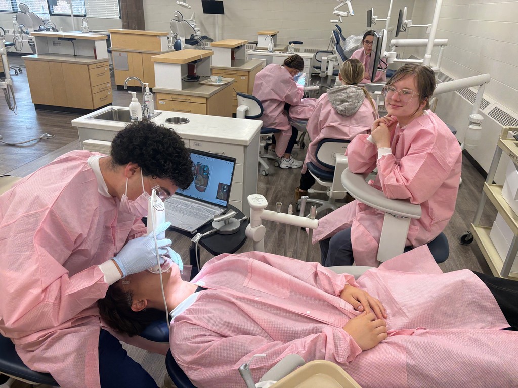 Student using a 3Shape TRIOS scanner to capture a 3D digital model/scan of classmate's teeth with another student observing them.