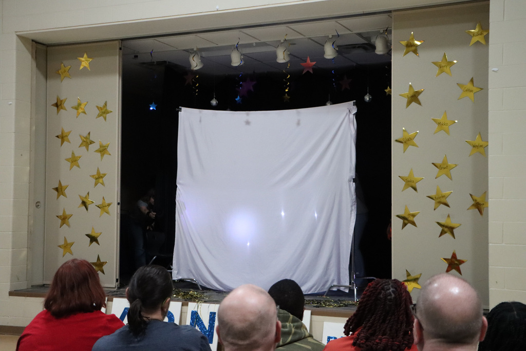 A group of students behind a white sheet and performing with flashlights. 