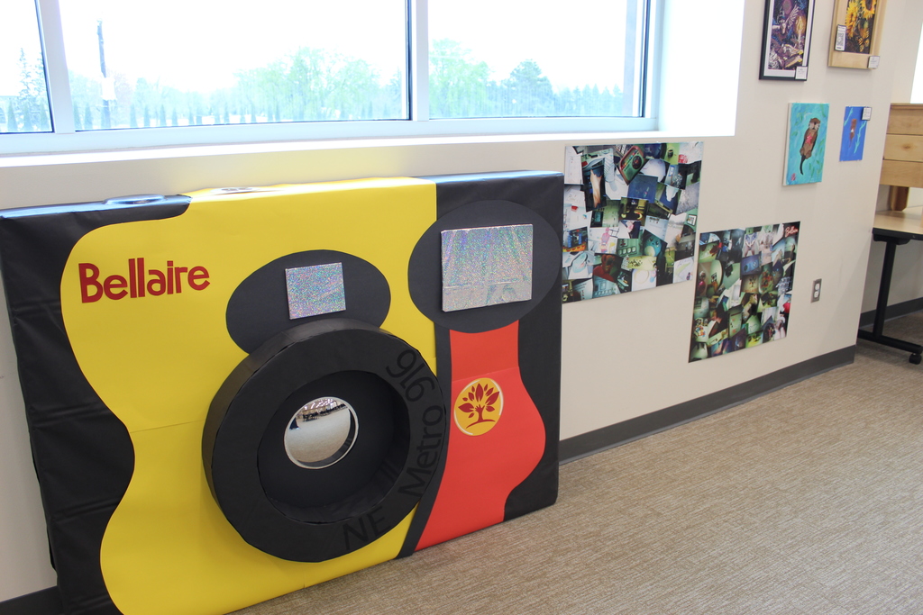 A big camera made from paper and cardboard with photos to the side of it.