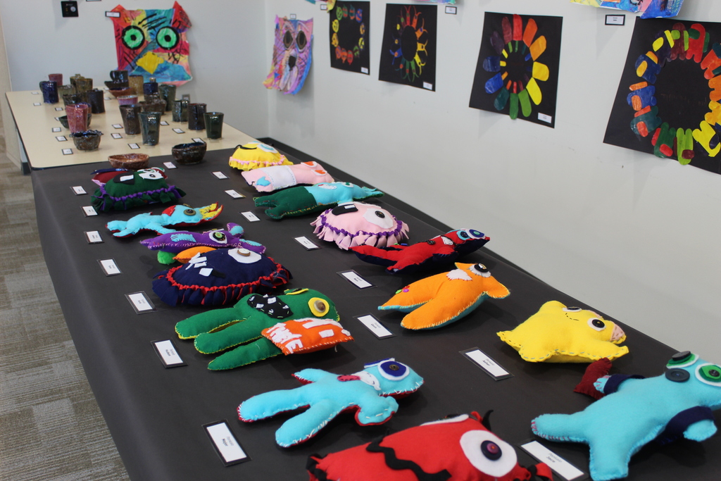 A table full of artwork that contains ceramic mugs and bowls and handmade plushies.