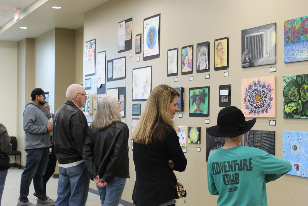 A group of people looking at student artwork on the wall.