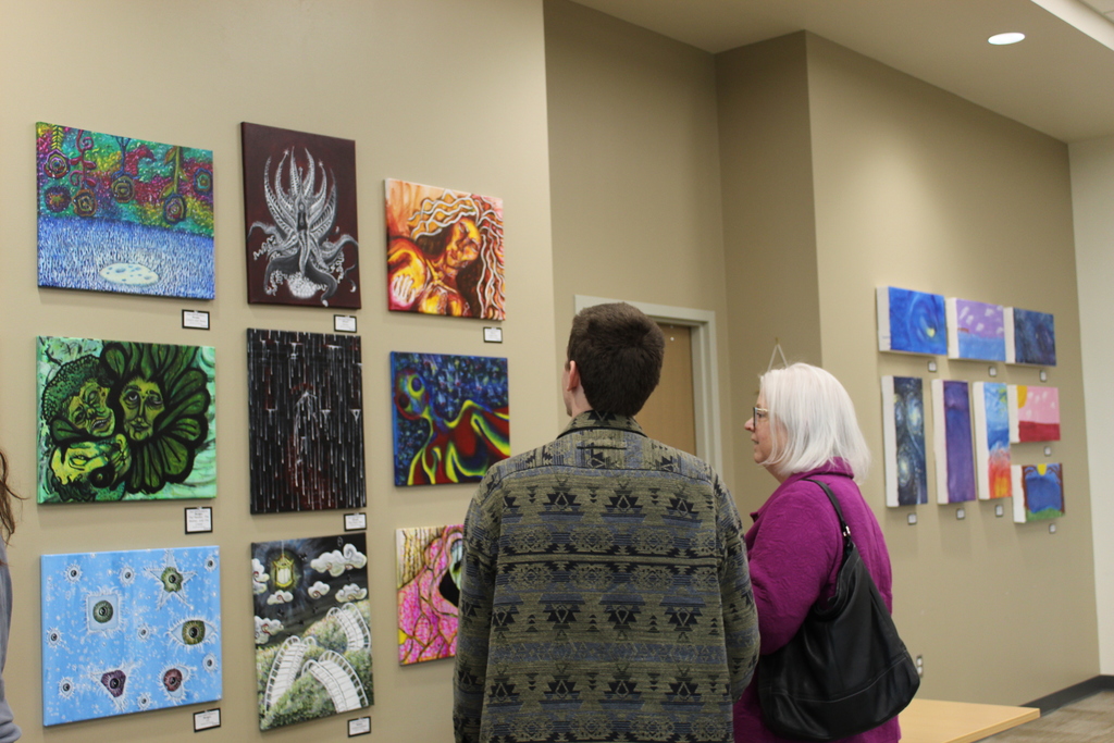 Two people looking at student artwork on the wall.