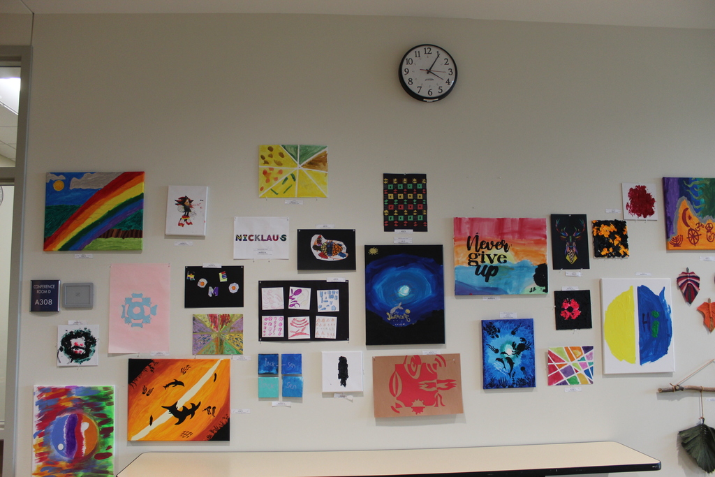 A wall of various student artwork hanging on a wall.