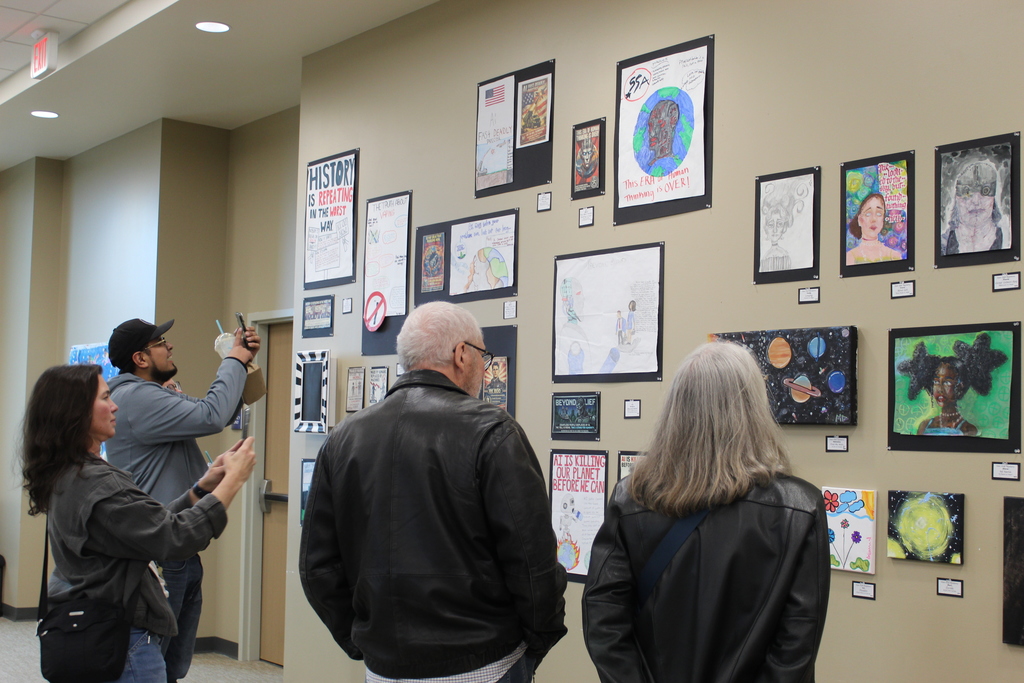 A group of people looking at student artwork on the wall.