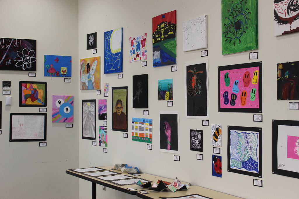 A wall full of various art from students and a table with other artwork as well.