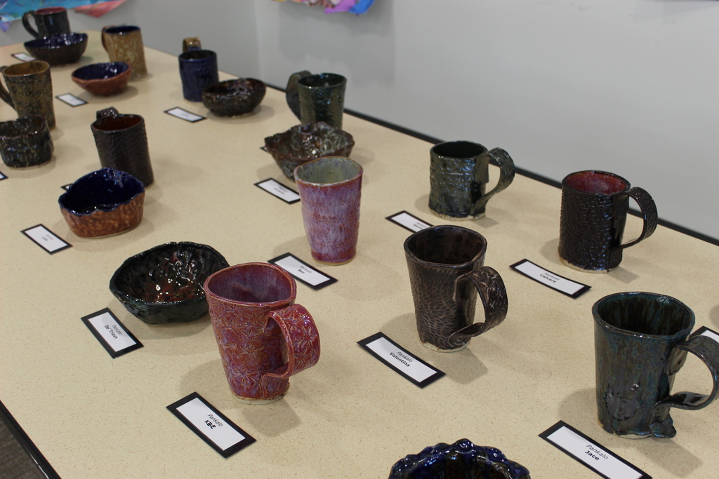 A table full of ceramic mugs and bowls made by students.