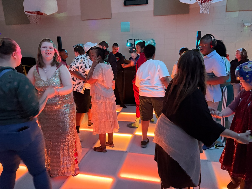 Students, staff, and family dancing on a lighted dance floor in the gym.
