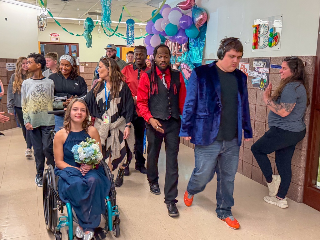 A group of students and staff doing the grand march with others cheering for them.
