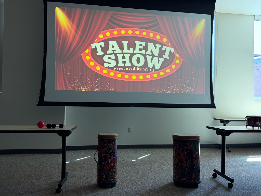 Image of a presentation screen that says "Talent Show Presented by Work Experience Life Skills" with tables and drums in front of the screen.