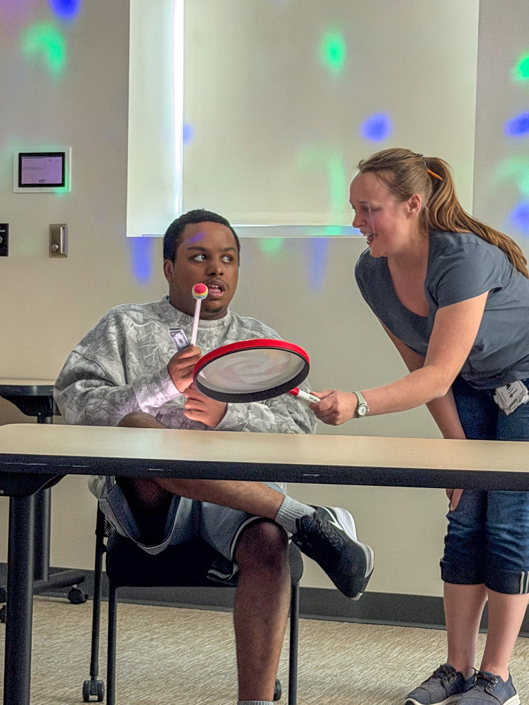 Staff holding a racket while a student uses a stick to tap at it. 