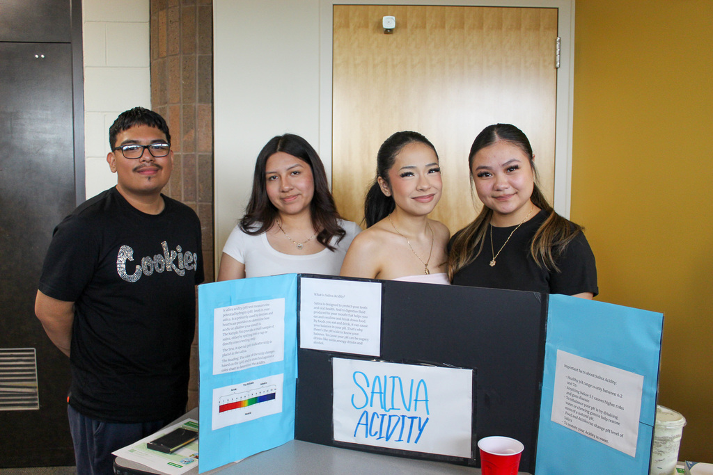 Students standing behind their presentation board and smiling. 