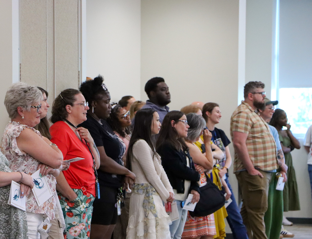Staff in the back of the room watching the student graduate give a speech.