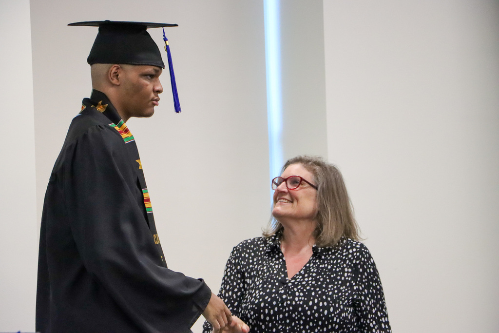 Graduate and staff shaking hands in celebration. 