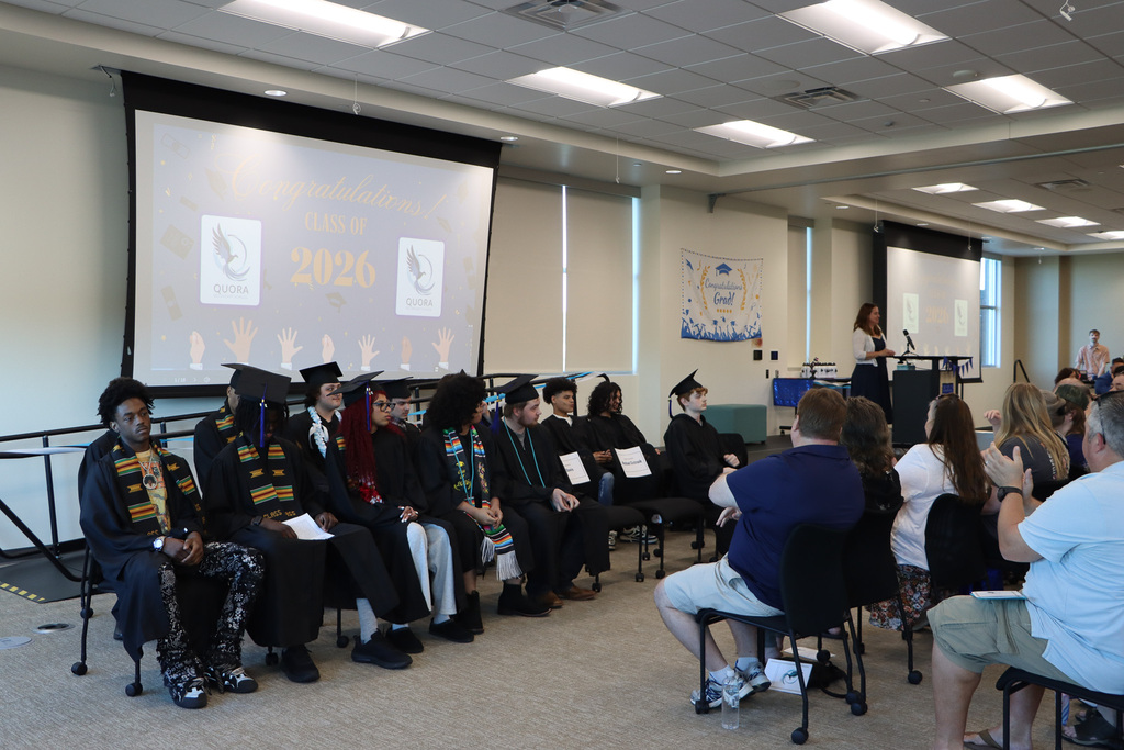 Student graduates, staff, and families listening to the principal give a speech.