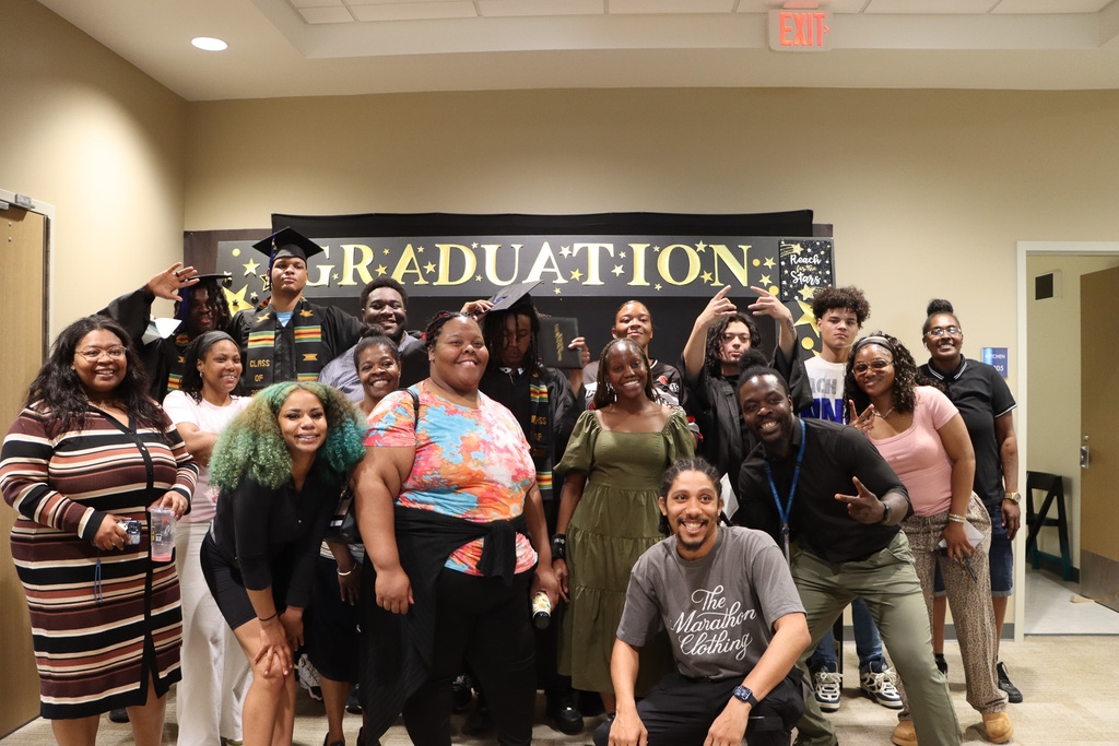 Group photo of staff and students smiling in front of the graduation sign.
