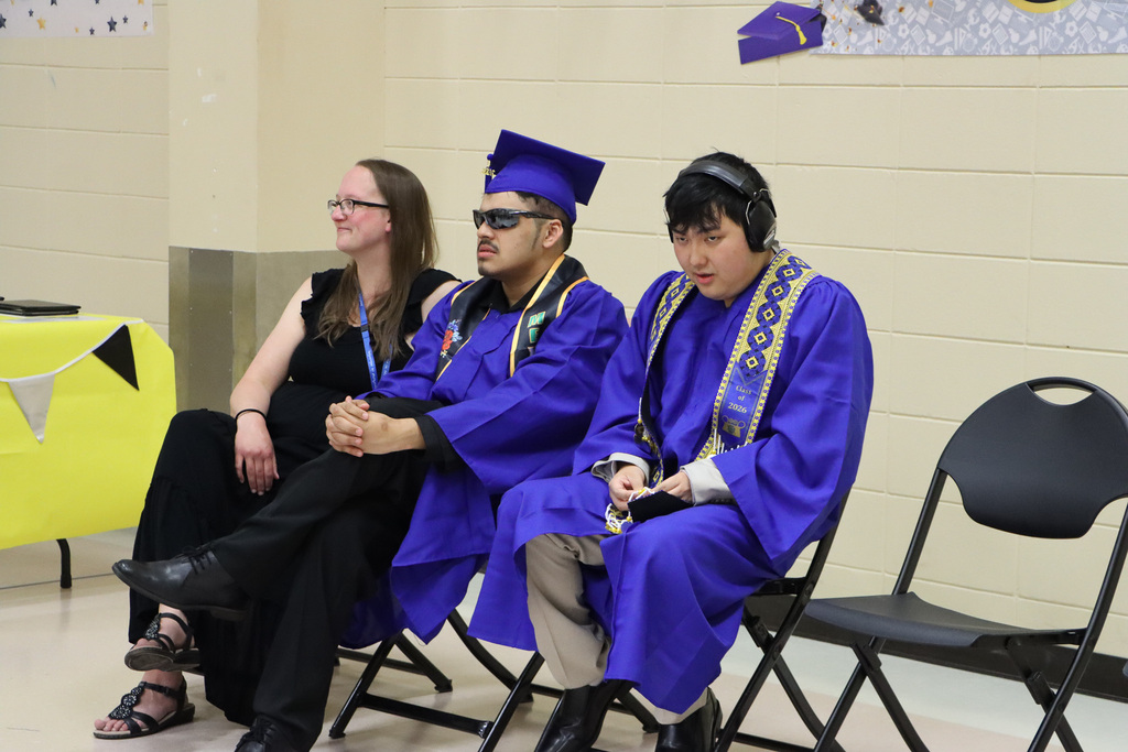 Staff and students in graduation gowns listening to the speaker. 