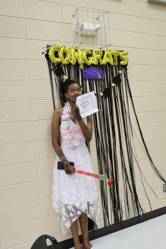 Student holding certificate and standing in front of backdrop that says, "Congrats."