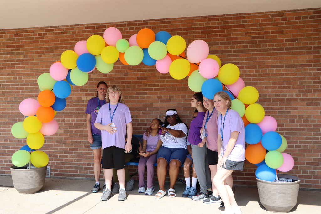 Students and staff taking a picture under an arch of balloons. 