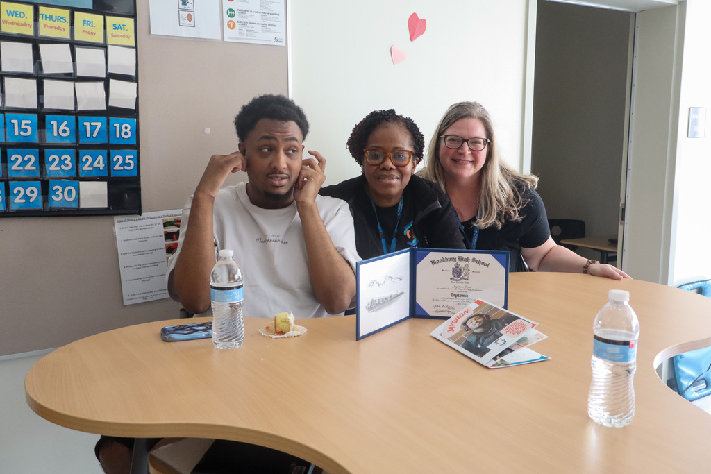 Staff and student sitting down at a table that has a diploma in celebration of the student graduating from school 