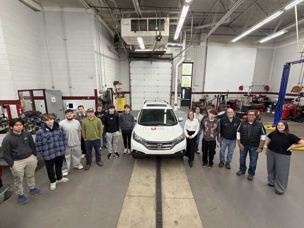 Group of students, staff, and community members standing around a donated vehicle.