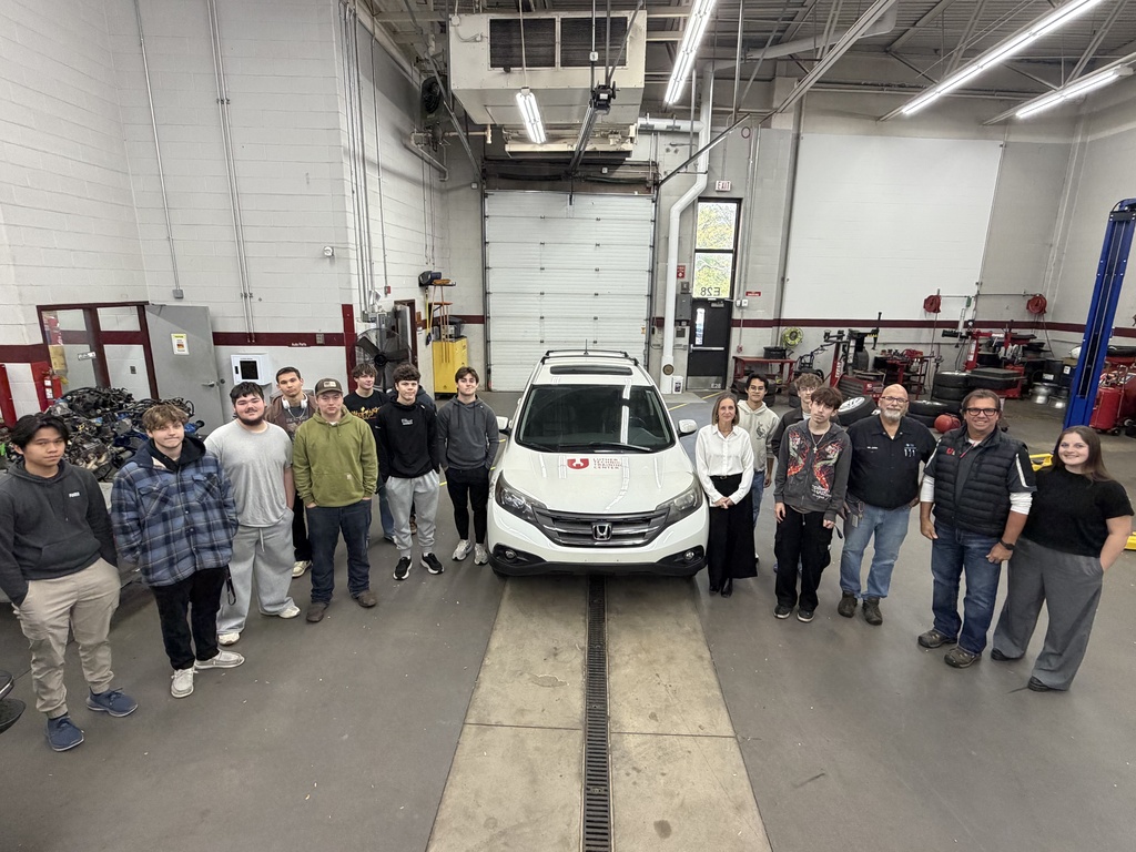 Group of students, staff, and community members standing around a donated vehicle.
