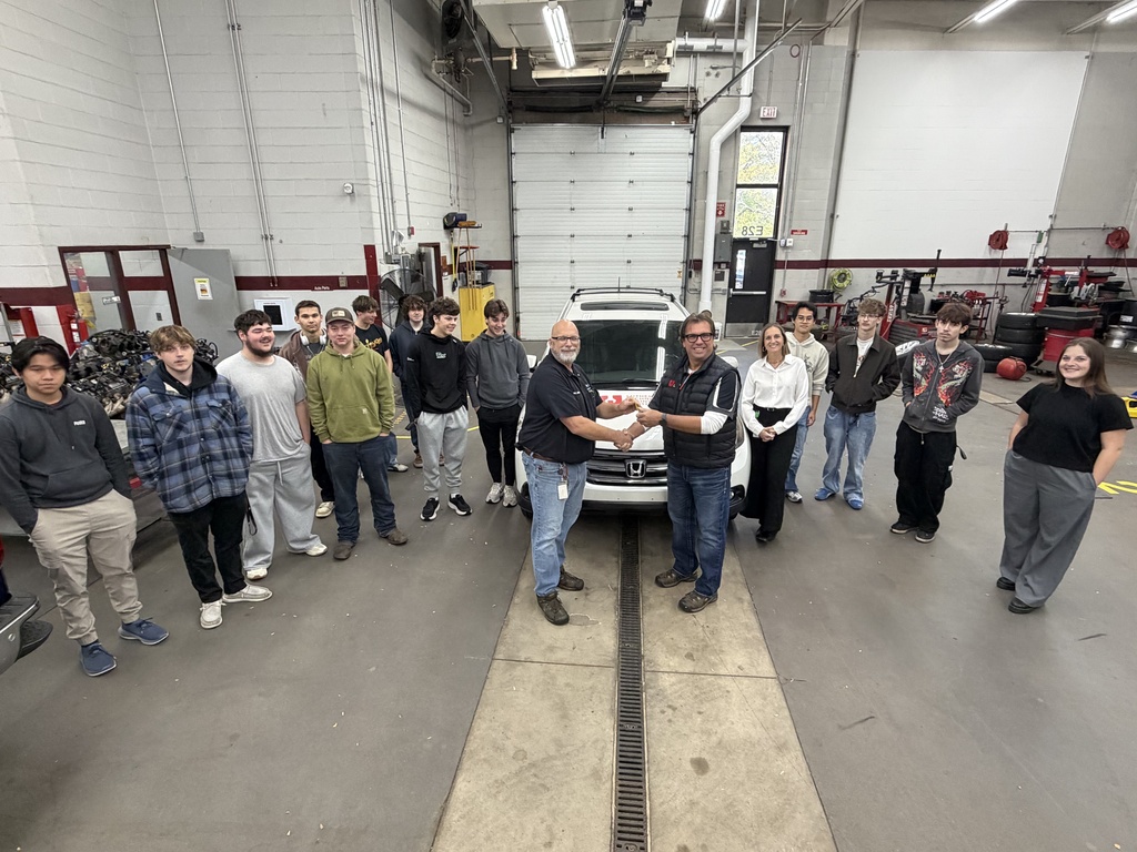 Group of students, staff, and community members standing around a donated vehicle.