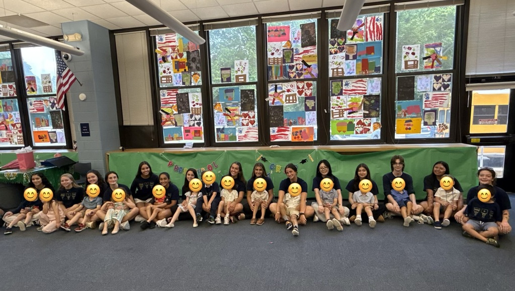 Several people seated on the floor with yellow smiley faces on their heads, in the library