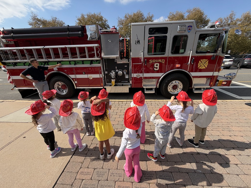 Several children in red hats gather around a fire truck with a person standing by it.