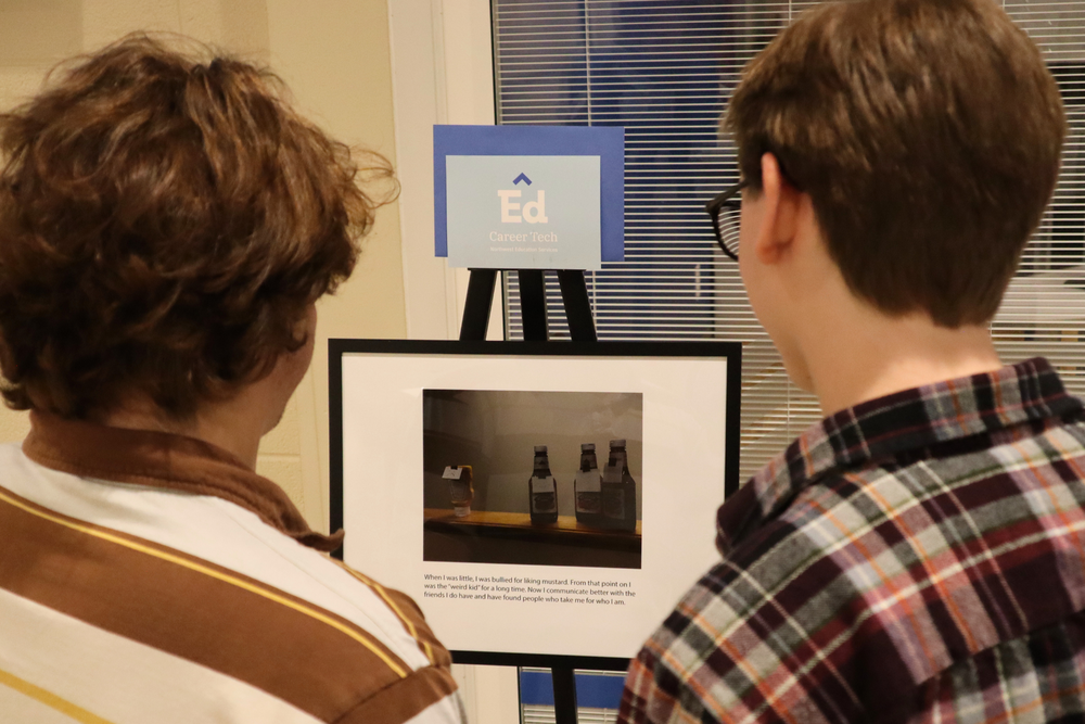 Two students view a photo placed on an easel during the Stories from a Stranger gallery event. 