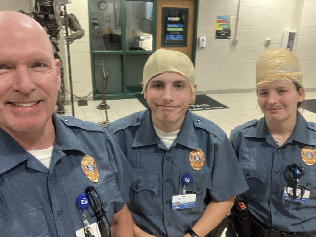 Image of Public Safety instructor Mr. Lennox posing with two students wearing bald caps.