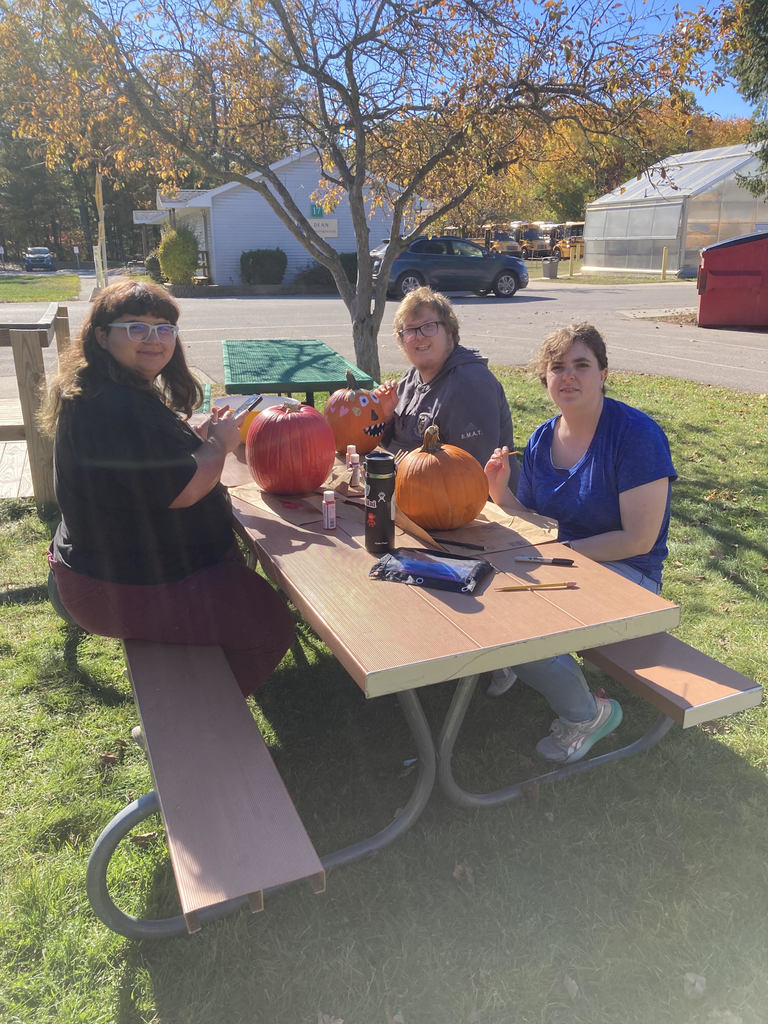 Image of three Adult Community Experience students painting pumpkins on a lunch table outside.