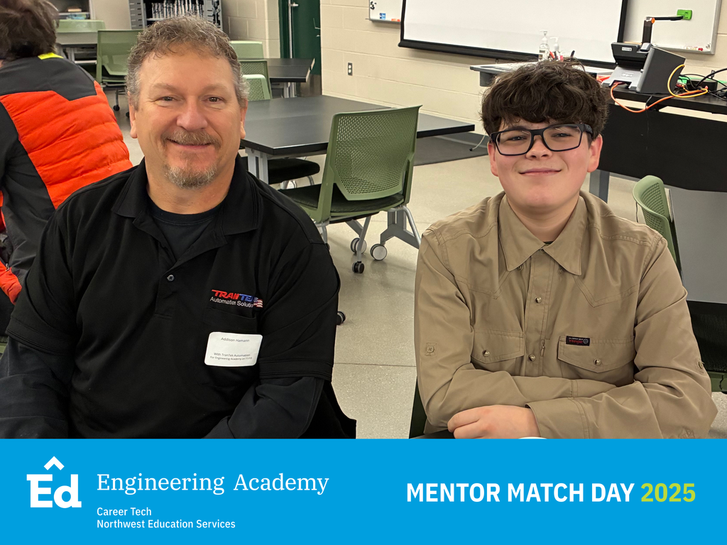 A close-up, seated portrait of an adult male mentor wearing a black polo shirt with an embroidered logo and name badge, and a teenage boy in a tan button-up shirt and glasses. They are smiling and sitting at a dark table in a classroom setting. The bottom of the image has a blue banner with the Northwest Education Services Career Tech Engineering Academy logo and white text: "MENTOR MATCH DAY 2025.”