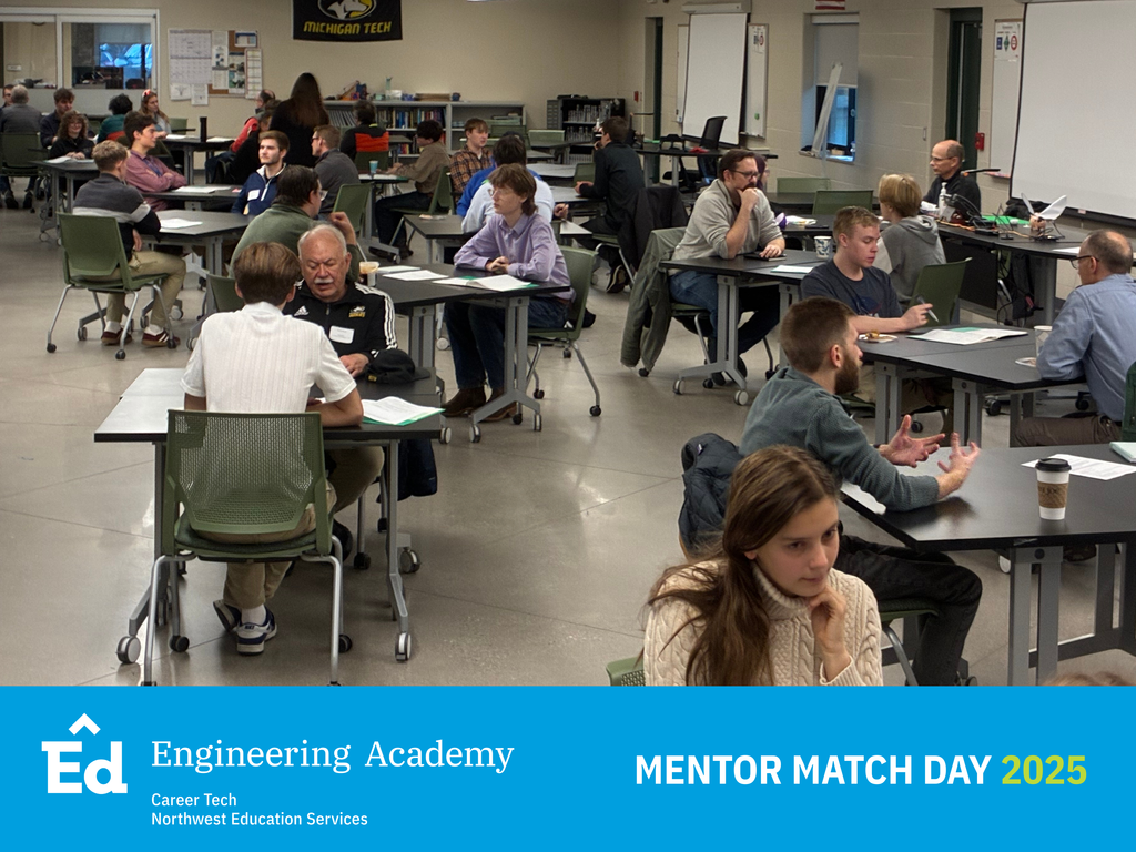A wide shot of a large classroom or multi-purpose room set up with multiple dark tables where mentors and students are engaged in various small group conversations. People are seated in green and black chairs throughout the room. The bottom of the image has a blue banner with the Northwest Education Services Career Tech Engineering Academy logo and white text: "MENTOR MATCH DAY 2025.”