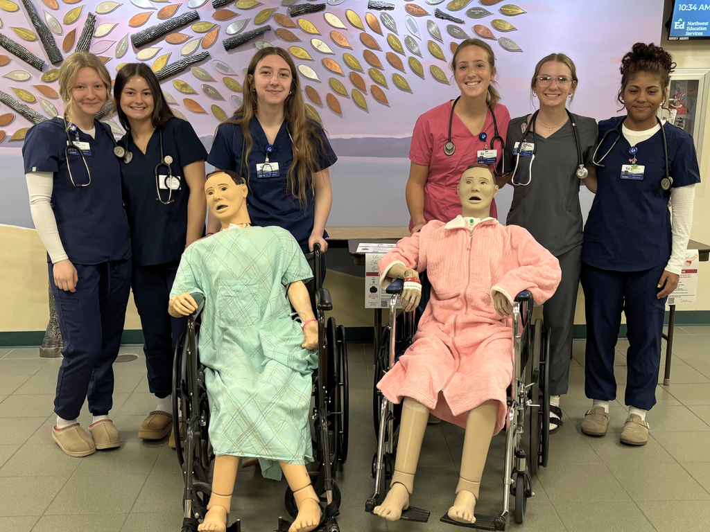Six Career Tech Health Sciences students posing with two practice manikins that were placed in wheelchairs.