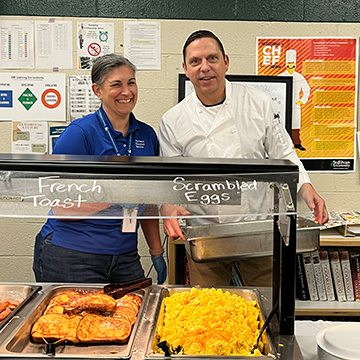 Two North Ed staff members posing behind a buffet of french toast and scrambled eggs. 