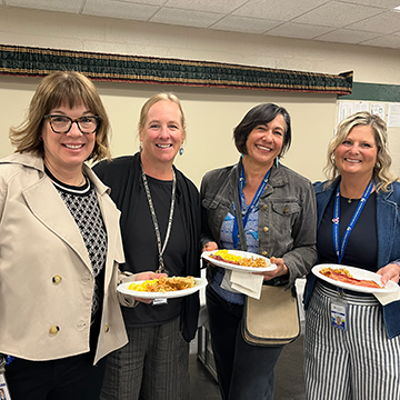 Image of four North Ed staff members smiling for a group photo, standing while holding their plates of food. 