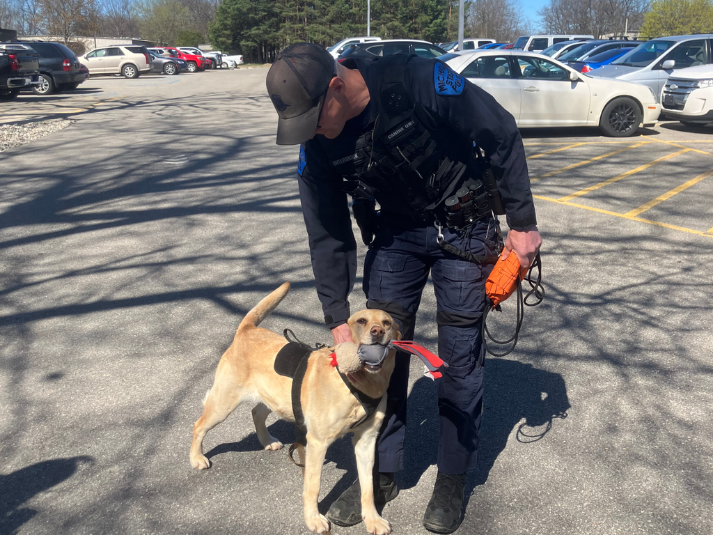 Michigan State Police Trooper Matthew Unterbrink and his dog Lulu standing in the North Ed Career Tech parking lot under a blue sky. 