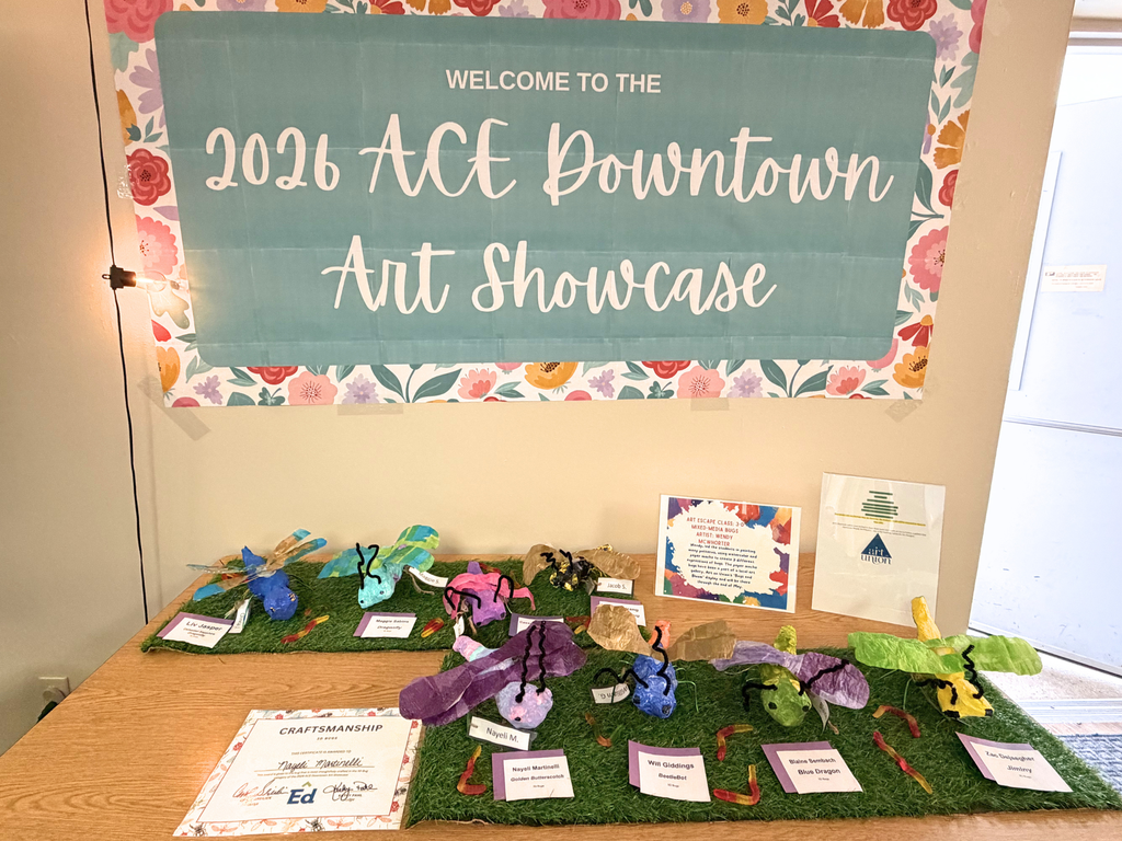 Photo: A table of paper mache insects with a poster reading, “Welcome to the 2026 ACE Downtown Art Showcase,” hanging on the wall above. 
