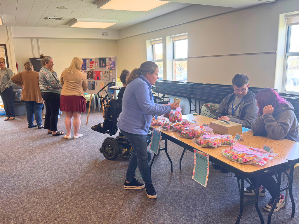 Photo: North Ed staff member purchasing baked goods from ACE students with art show attendees in the background. 