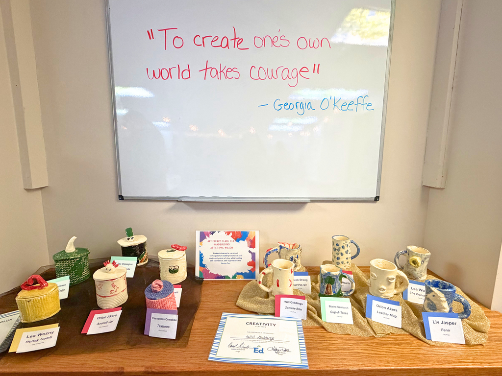 Photo: A table filled with clay pottery artwork and a white board with the Georgia O’Keefe quote, “To create one’s own world takes courage,” hanging on the wall above. 
