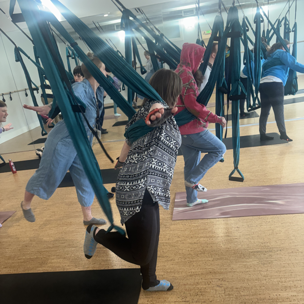 A class of North Ed students striking yoga poses while being supported by trapeze apparatuses around their limbs. 