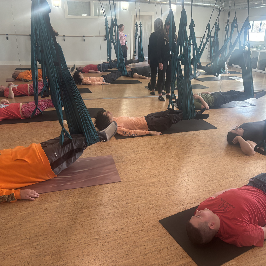 A class of North Ed students laying on their backs on yoga mats with their legs suspended in the air.