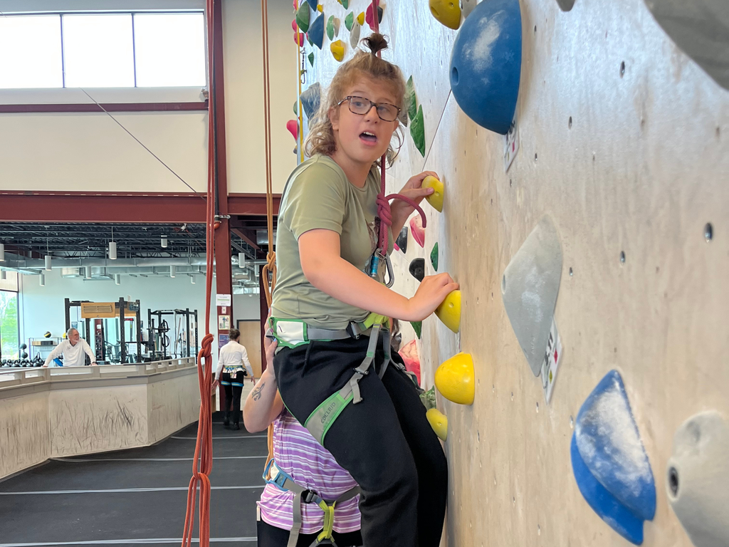 Student looking at camera while being supported by an adult during rock climbing activity. 