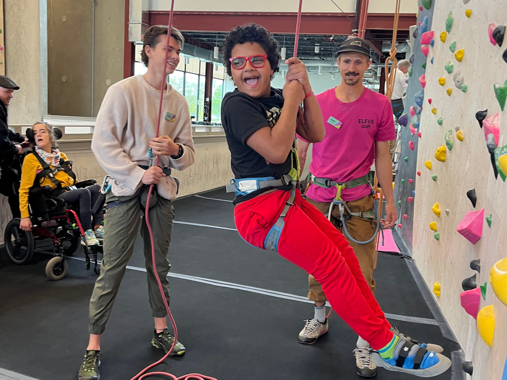 Student smiling while suspended from ceiling while rock climbing. 