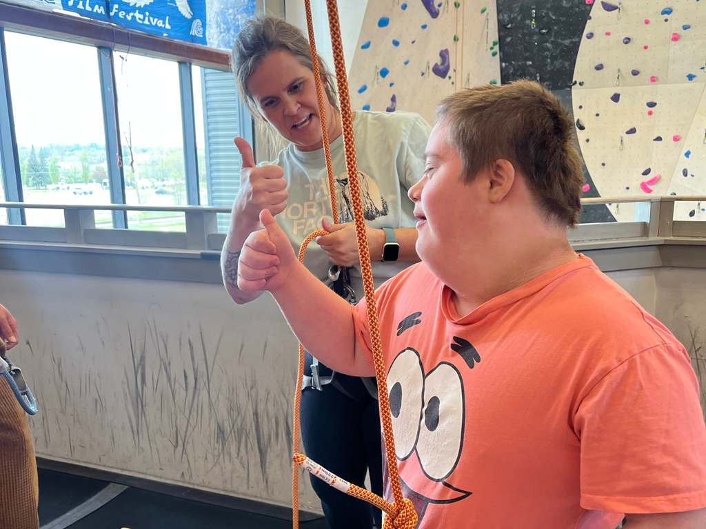 Student giving an adult a thumbs up at Elev8 rock climbing gym. 