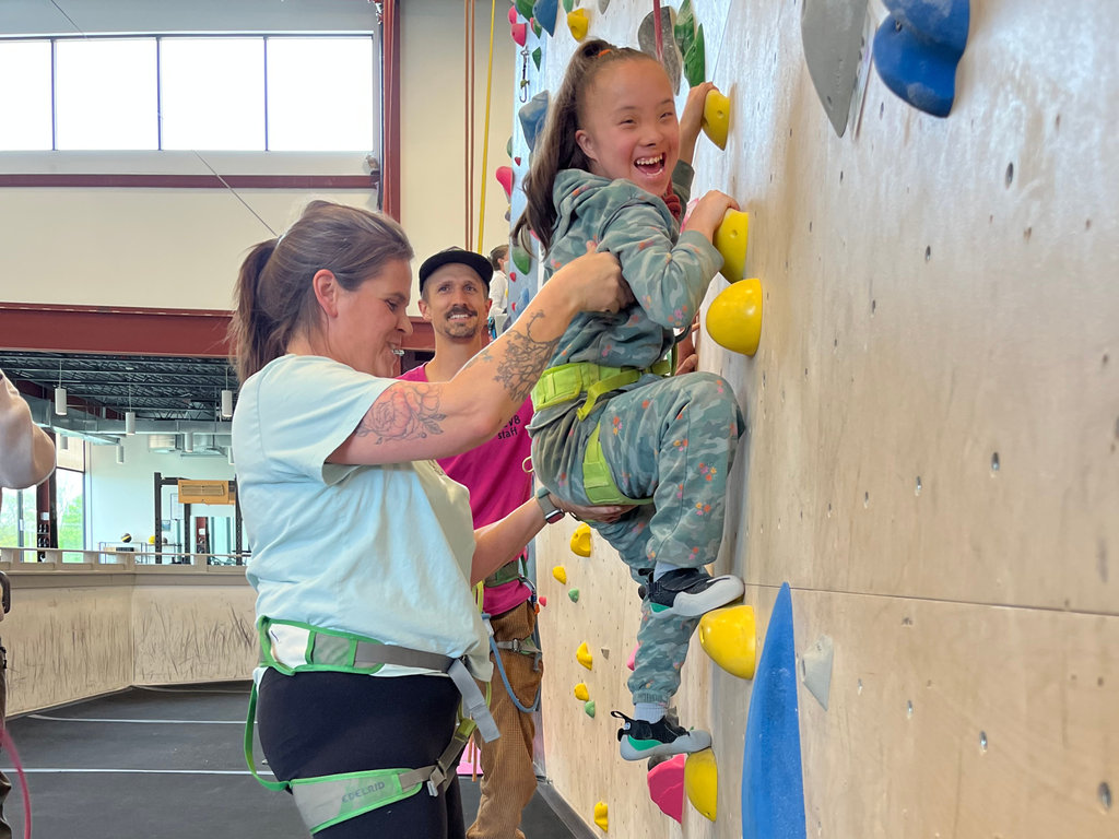 Adult helping smiling student rock climb. 