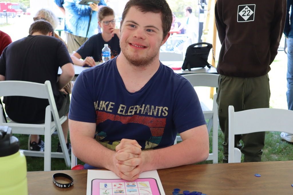 Transition Campus student sitting and smiling with a bingo card at the annual picnic.