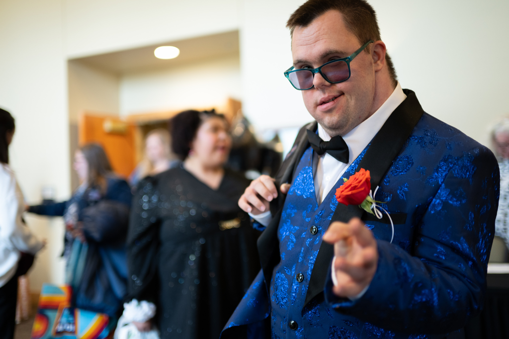 Transition Campus student wearing a blue tuxedo and tinted glasses, gesturing to the camera at prom.