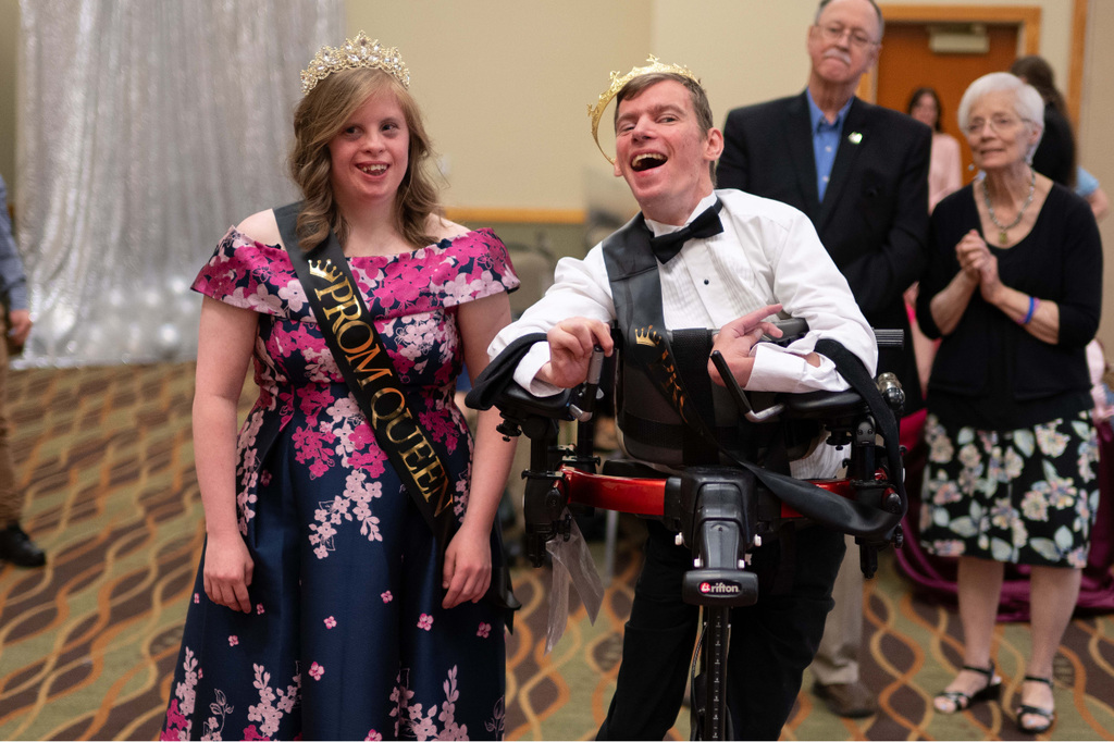 Transition Campus Prom King and Queen posing for a photo with proud family members applauding in the background.